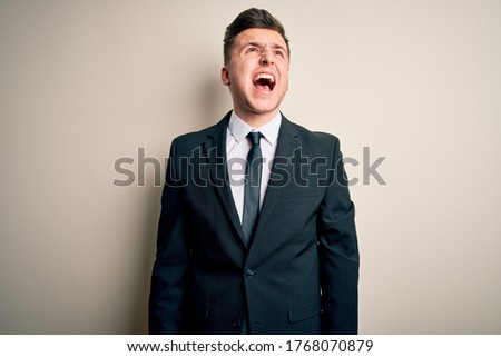 Young handsome business man wearing elegant suit and tie over isolated background angry and mad screaming frustrated and furious, shouting with anger. Rage and aggressive concept.