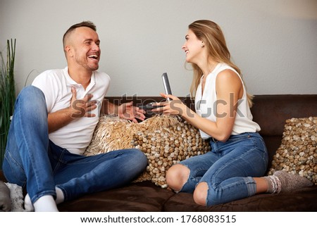 Beautiful young girlfriend giving wristwatch to surprised boyfriend while sitting on sofa at home