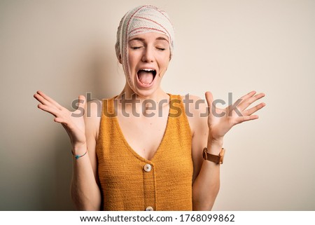 Young beautiful redhead woman injured for accident wearing bandage on head celebrating mad and crazy for success with arms raised and closed eyes screaming excited. Winner concept