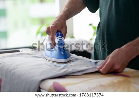 A man ironing clothes, the owner in the house puts things in order, a hot iron in the hands of her husband.
