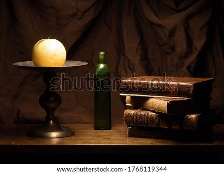 Still Life Candle Candlestick Old Green Bottle Leather Gold Gild Books Dark Brown Fabric Background Wood Table Royalty-Free Stock Photo #1768119344