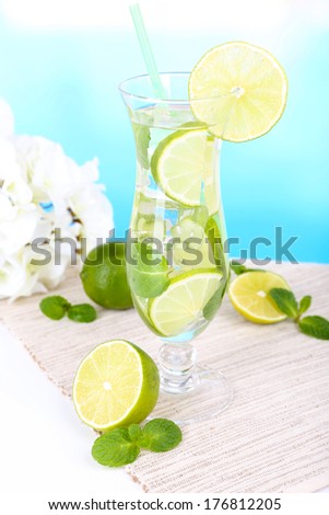 Glass of cocktail with lime and mint on table on light blue background