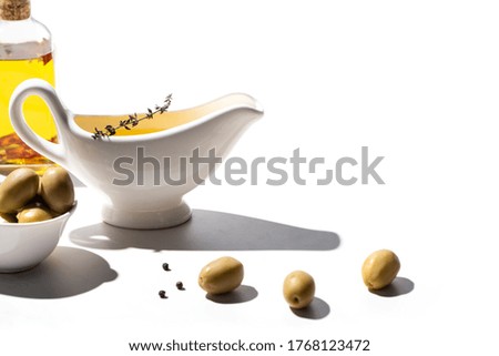 olive oil in bottle and sauce boat near green olives and black pepper on white background