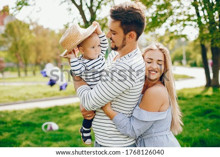 A young and beautiful blonde mother in a blue dress, along with her handsome man dressed in a white jacket, playing with her little son in the summer solar park