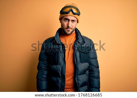 Young handsome skier man with beard wearing snow sportswear and ski goggles skeptic and nervous, frowning upset because of problem. Negative person.