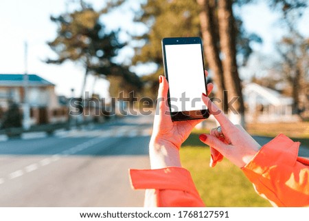A woman's hands holds a smartphone, and presses the screen, hand close-up. In the background, the city road is blurred. Mock up. Concept of modern technologies, business and app for the phone