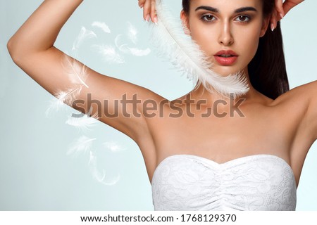 Armpit epilation, hair removal. Young woman holding her arms up and showing clean underarms, depilation smooth clear skin . Beauty portrait. armpit's care. Large white feather near skin Royalty-Free Stock Photo #1768129370