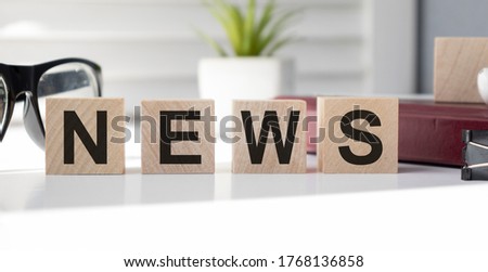 Eyeglasses on wood cube which have text NEWS lay on newspaper.