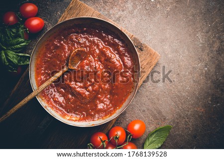 Classic homemade Italian tomato sauce with basil for pasta and pizza in the pan on a wooden chopping board on brown background, top view. Royalty-Free Stock Photo #1768139528