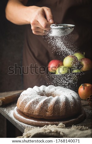 Rustic Style Apple Bundt Cake Sprinkled with Icing Sugar on old wooden table with woman hands