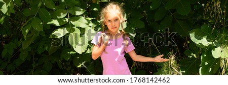 a cute little six year old kid girl poses against a background of green leaves of tree during his summer vacation. banner
