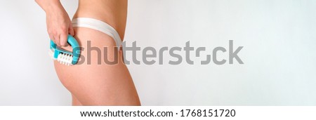 Bodycare. Anti cellulite massage. Woman wearing white panties massaging her hip using a massage roller on a white background, slimming for the beach sea summer season