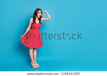 Full length photo of attractive lady hold arm under eyes look far away traveler need walk long way wear red white dotted retro dress summer open toe shoes isolated blue color background
