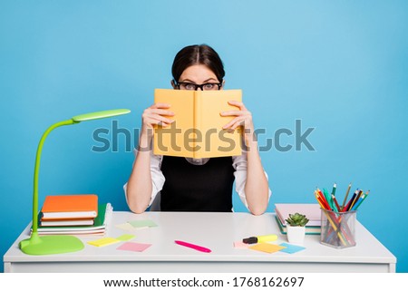 Photo of astonished high school girl sit table close cover face copybook hide herself from graduate exam preparation wear black white stylish overall uniform isolated blue color background