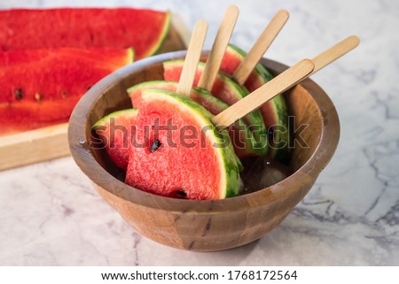 Watermelon slices on sticks with ice cubes. Fresh watermelon popsicles in wooden bowl.