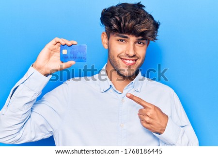 Young hispanic man holding credit card smiling happy pointing with hand and finger 