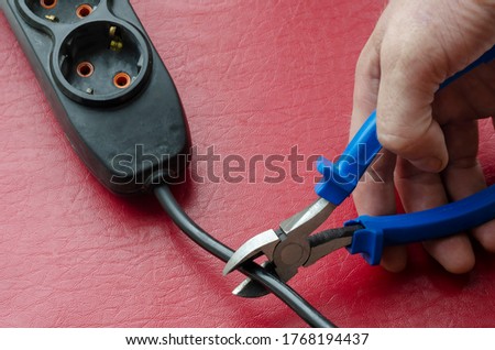 Hand cut the cable of the electric splitter with pliers. The electrician makes an emergency disconnection of the consumer from the mains. Electrical safety.