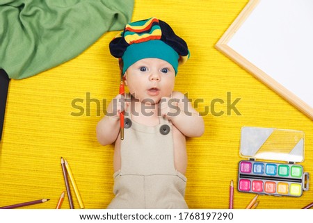 Funny little boy lie on the floor and draw with pencils. Works of child. Studio shot top view of child lying on yellow background. Baby healthy, happiness, active leisure, childhood lifestyle concept