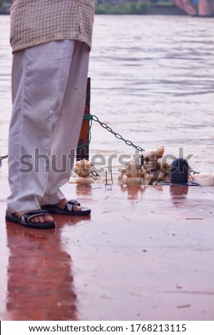 A man feet wearing white pijama and indian footwear standing by Ganga river and God sculpture in Haridwar, India