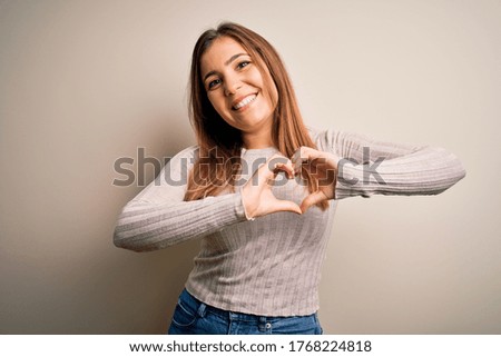 Beautiful young woman standing casual over isolated background smiling in love showing heart symbol and shape with hands. Romantic concept.