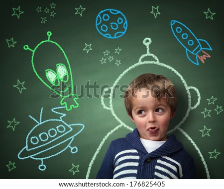Imagination and dreams of a child, dressed as a space man in front of a blackboard with chalk drawings of space rocket and alien, concept for aspirations and daydreaming