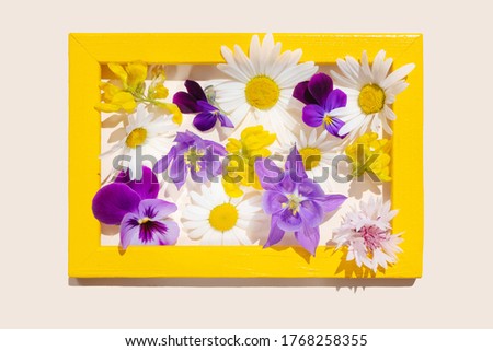 Homemade yellow photo frame with various yellow, purple and pink flowers inside. Cute summer concept. Image for holiday cards, greetings. Isolated, light background