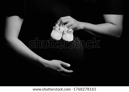 husband's hand puts baby shoes on the belly of his pregnant wife