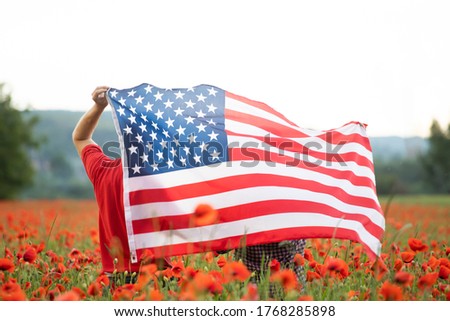 Young couple holding Flag of the United States in beautiful summer field on a clear, sunny day. Celebrating Independence Day, National holiday concept.