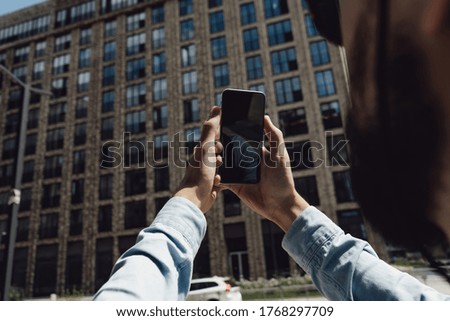 Tourist man in hat travels around the city. A guy with a backpack and sunglasses. The traveler stopped to take a photo on phone. Hipster with a beard. Communication technology in an urban environment.