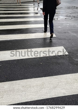 Legs of city dweller crossing wet asphalt road at pedestrian zebra crosswalk after rain