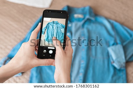Woman taking photo of denim shirt on smartphone  Royalty-Free Stock Photo #1768301162