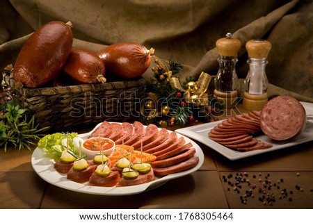 Still life of many and different food products, such as ham, salami, carrots, pickles and sauces, with some Christmas decorations.