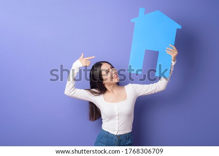 Portrait of beautiful woman  is holding blue  home on purple background 