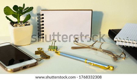 Glasses, notepad, smartphone, flower, pen, paper clips on a light background. Workplace close up.