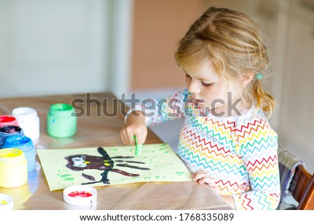 little creative toddler girl painting with finger colors an owl bird. Child having fun with drawing at home, in kindergarten or preschool daycare. Games, education and distance learning for kids.