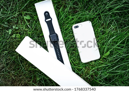 Smart watch and mobile phone on grass background.