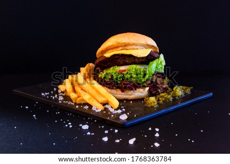 Burger served with crispy french fries on stone plate with dark background and rock salt as garnish.