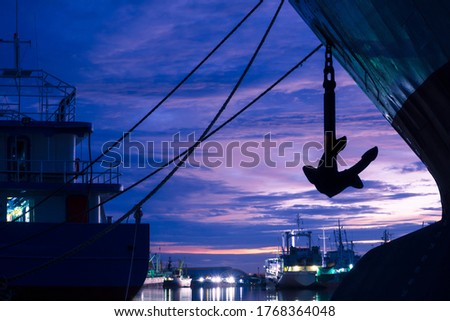 Silhouette mooring rope with anchor of cargo ships docked at port on riverside against twilight sky background 