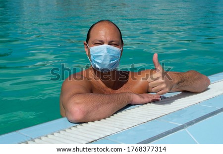 Young man enjoying swimming and bathing in open air outdoor swimming pool with n95 face mask. Keeping social distancing, protecting health during corona virus pandemic 