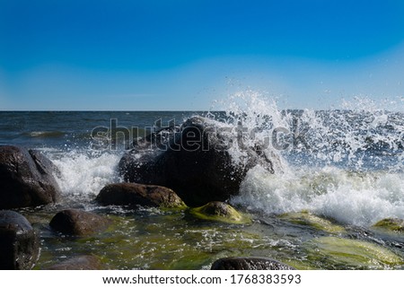 Waves hitting against the rocks. Baltic sea on sunny summer day. Little moss on the stones. Nice foam and bubbles everywhere. Amazing high resolution quick shutterspeed shots. Blue cloudless sky. Warm