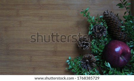 Autumn decoration with apple, pine cones, green branches and nuts on the light brown wood background. Concept of Autumn season.    