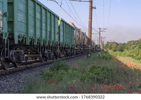 Freight train movement on the railway paths along blooming poppies. Freight railway carriages in the industrial area.