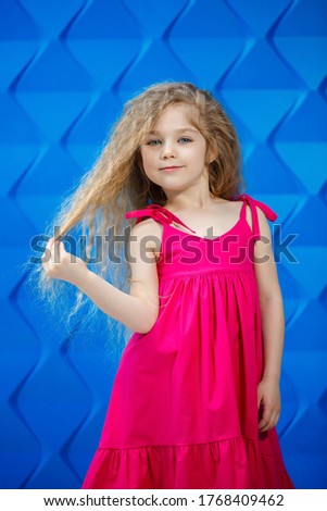 Fair-haired little girl in a pink dress on a blue background dancing and laughing, bright children's emotions of joy, happy childhood
