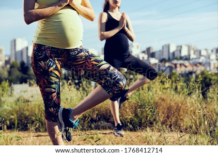 Two pregnant women standing in tree yoga position outdoors.