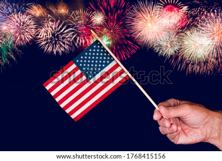 Senior mans hand holding a small toy USA flag and cutout against fireworks background
