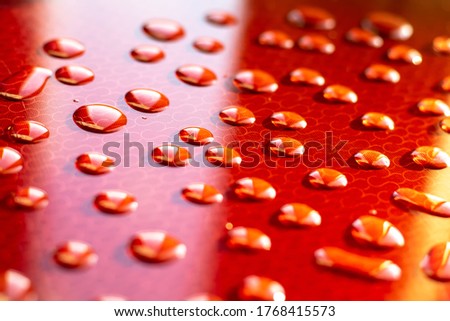 Large drops of transparent water on a red background sparkling in the sun. Close-up.