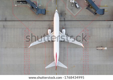 Top down view on comercial airplane docking in terminal in the parking lot of the airport apron, waiting for services maintenance, refilling fuel services after airspace lock down. Modern airliner Royalty-Free Stock Photo #1768434995