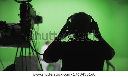 Film crew in green studio shooting video. Chroma - technology of combining two or more images or frames in single composition. Cameraman,director,crew. Filmmaking industry.
