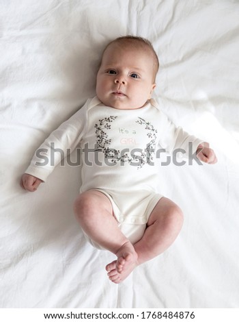 Portrait of a newborn baby girl who lies on a bed. Three-month-old girl in white suit lies on a veil view from above. High quality photo Royalty-Free Stock Photo #1768484876