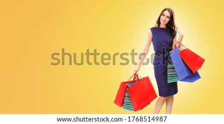 Portrait picture of happy woman with shopping bags, standing over orange yellow background, with copy space for some slogan, advertising or text message. Sales or client costumer bank credit concept.